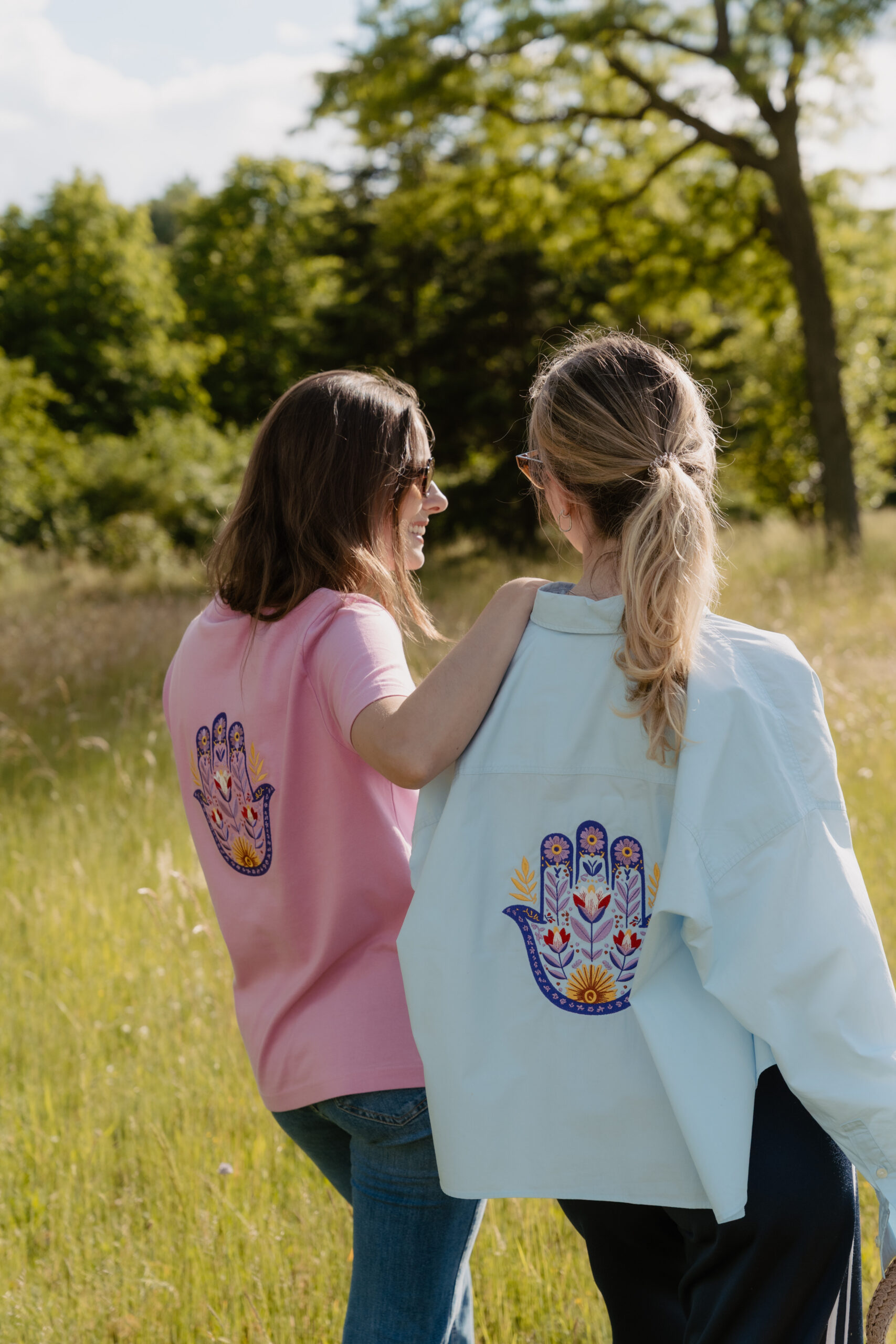Zwei Personen mit einem farbig gestickten Handmotiv auf T-Shirt und Overshirt