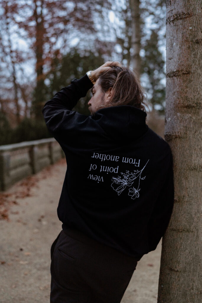 Mann in schwarzem Hoodie mit weißer Schrift- und Blumenstickerei auf dem Rücken